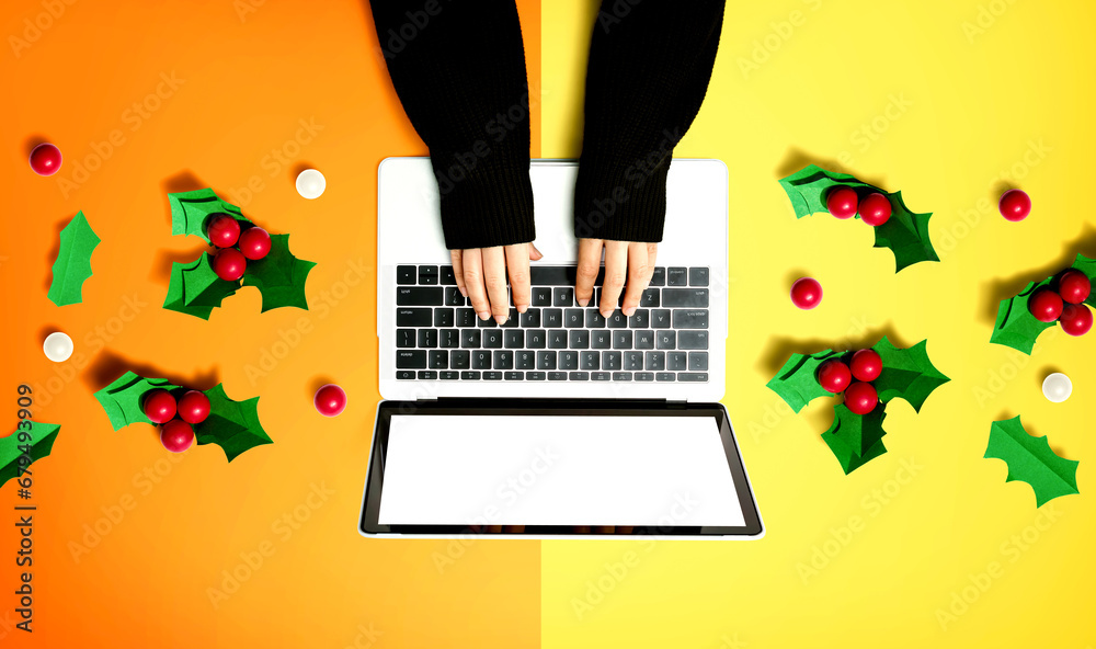 Person using a laptop computer with Christmas holly berries from above