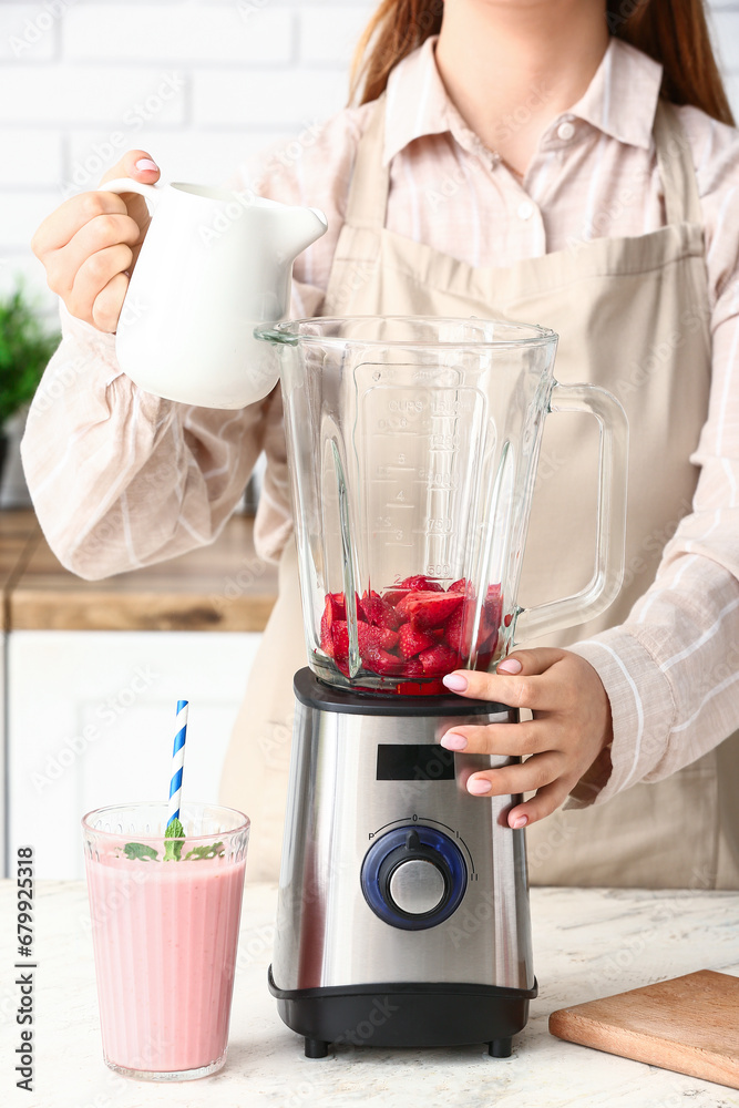 Woman preparing tasty strawberry smoothie with blender at table in kitchen