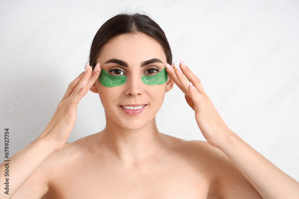 Pretty young woman with under-eye patches on light background