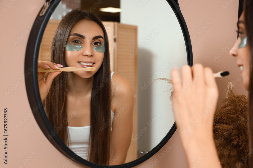 Young woman with under-eye patches brushing teeth in bathroom