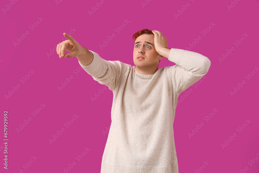 Scared young man pointing at something on purple background