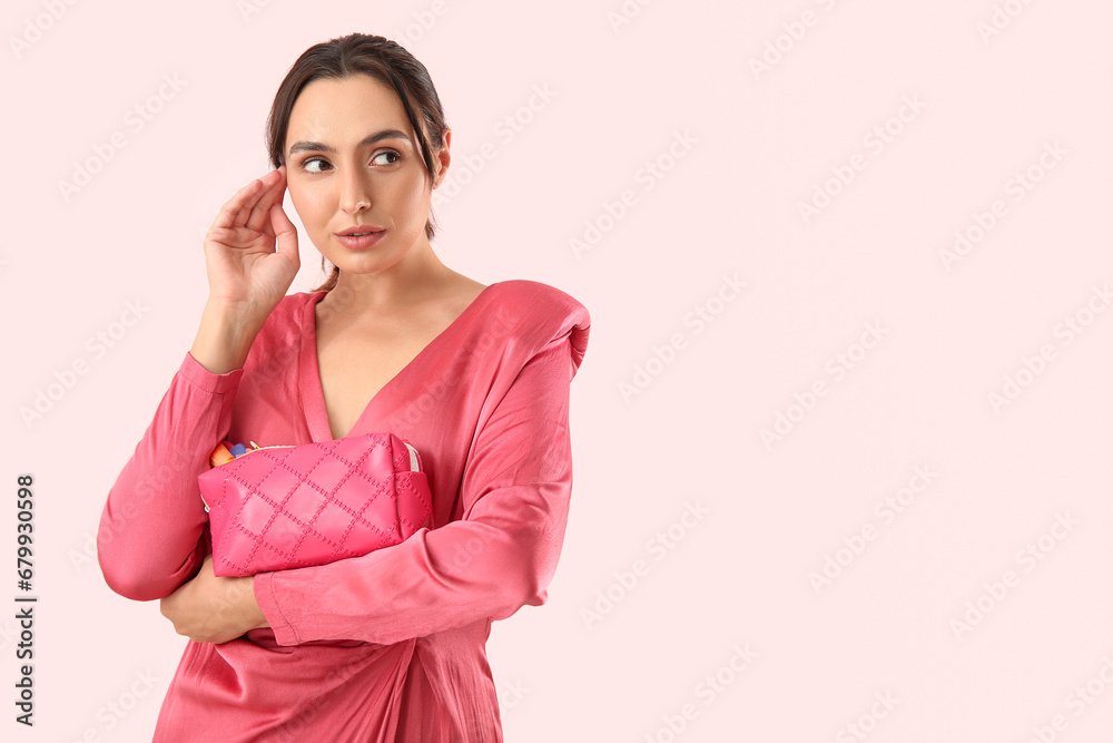 Beautiful young woman with cosmetic bag full of makeup products on pink background