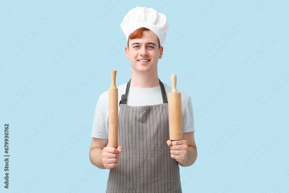 Male confectioner in apron with rolling pins on blue background