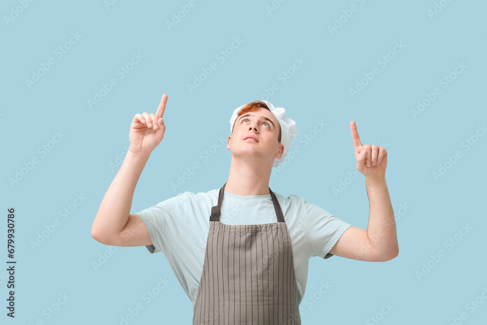 Male confectioner in apron pointing at something on blue background