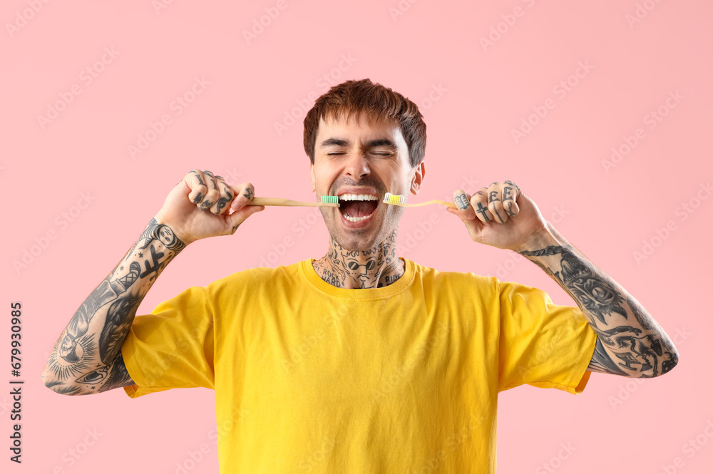 Young tattooed man with toothbrushes on pink background