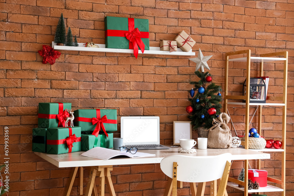 Modern workplace with blank laptop, presents and Christmas tree in office