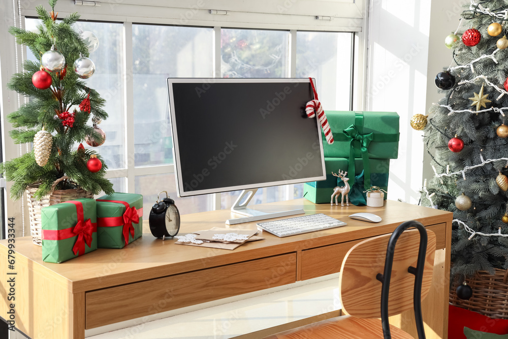 Workplace with computer monitor, presents and Christmas tree in office