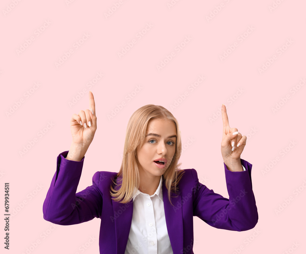 Young shocked businesswoman pointing at something on pink background. Business idea concept