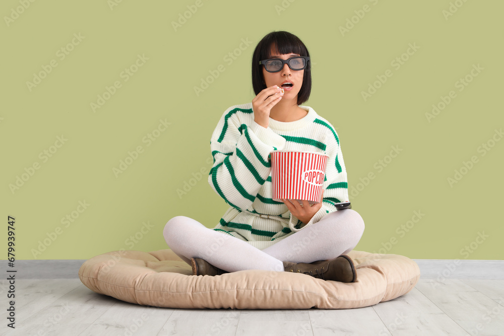 Young woman in 3D glasses with popcorn watching TV near green wall