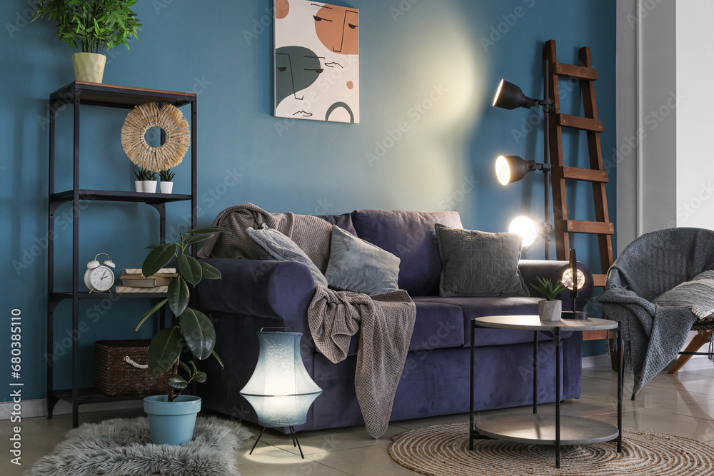 Interior of dark living room with blue sofa and glowing lamps