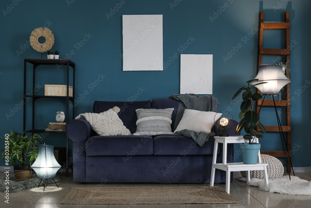 Interior of dark living room with blue sofa and glowing lamps