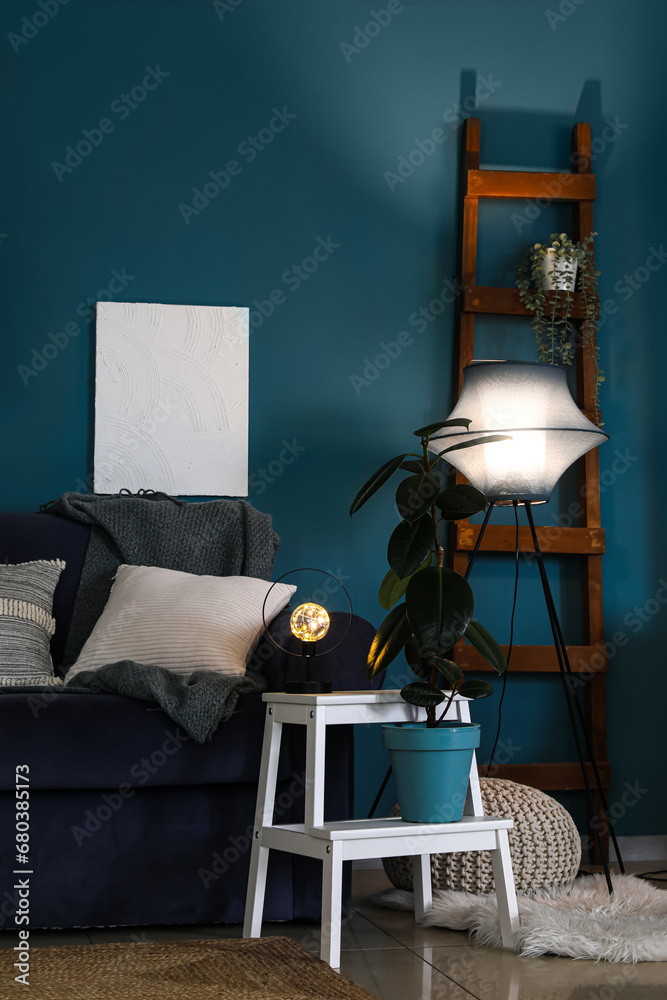 Interior of dark living room with blue sofa and glowing lamps