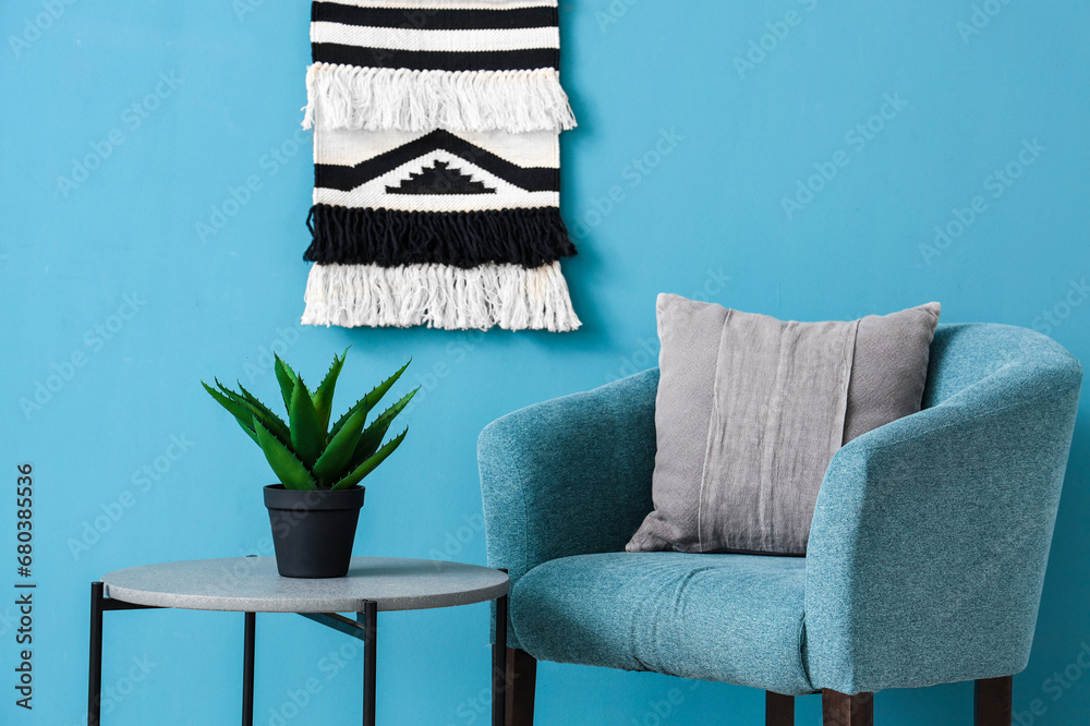 Cozy armchair and coffee table with houseplant near blue wall