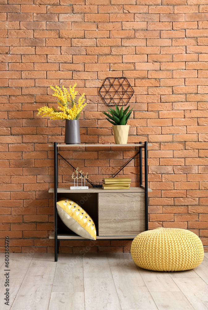 Shelving unit with different houseplants and books near brown brick wall