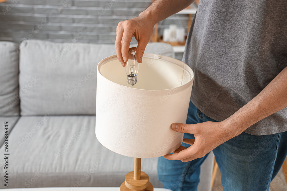 Man changing light bulb in table lamp at home, closeup