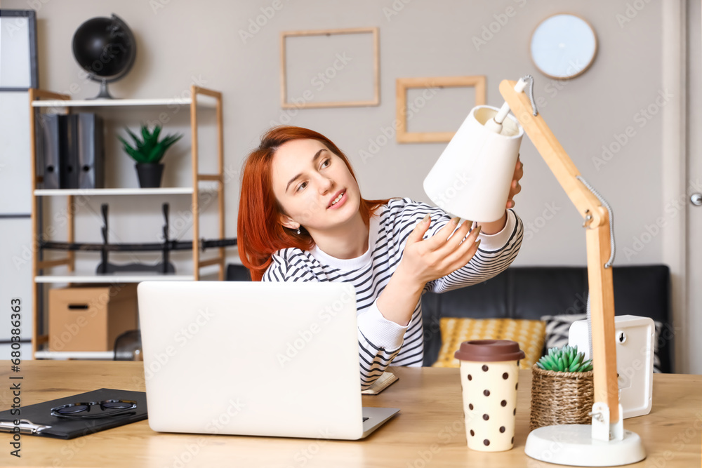 Pretty young woman changing light bulb in desk lamp at home