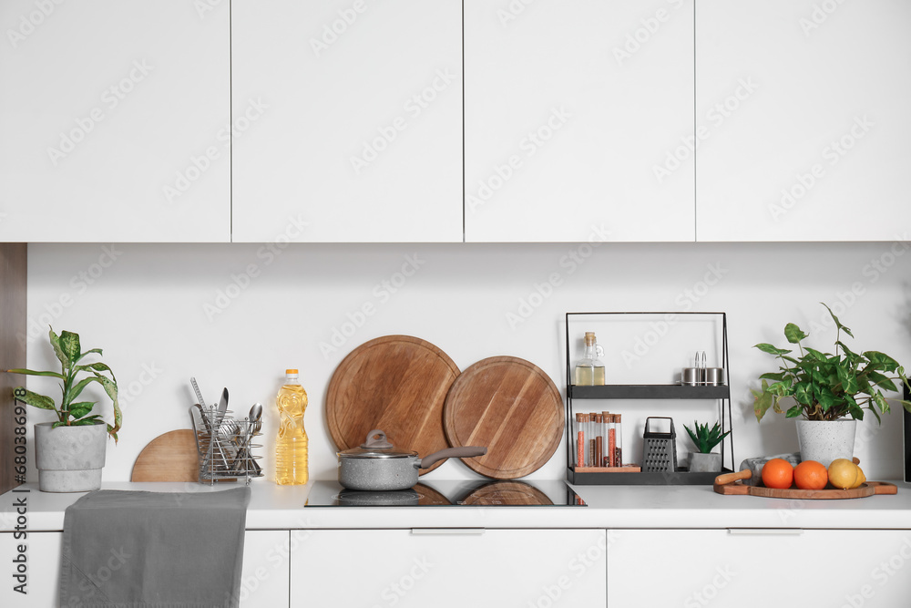 Electric stove with cooking pot and utensils on white counter in modern kitchen