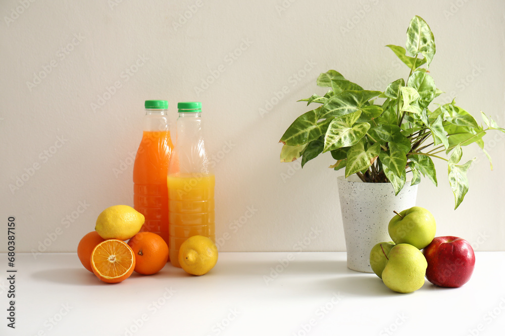 Bottles of juice, fresh fruits and houseplant on white kitchen counter