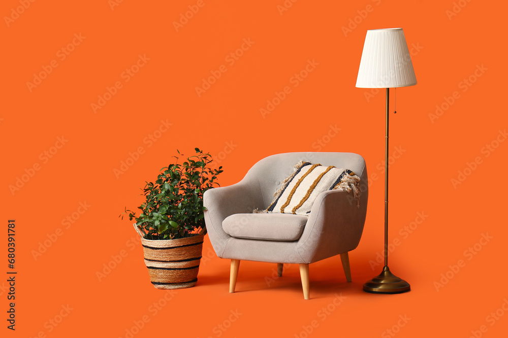 Modern grey armchair with lamp and flowerpot on orange background