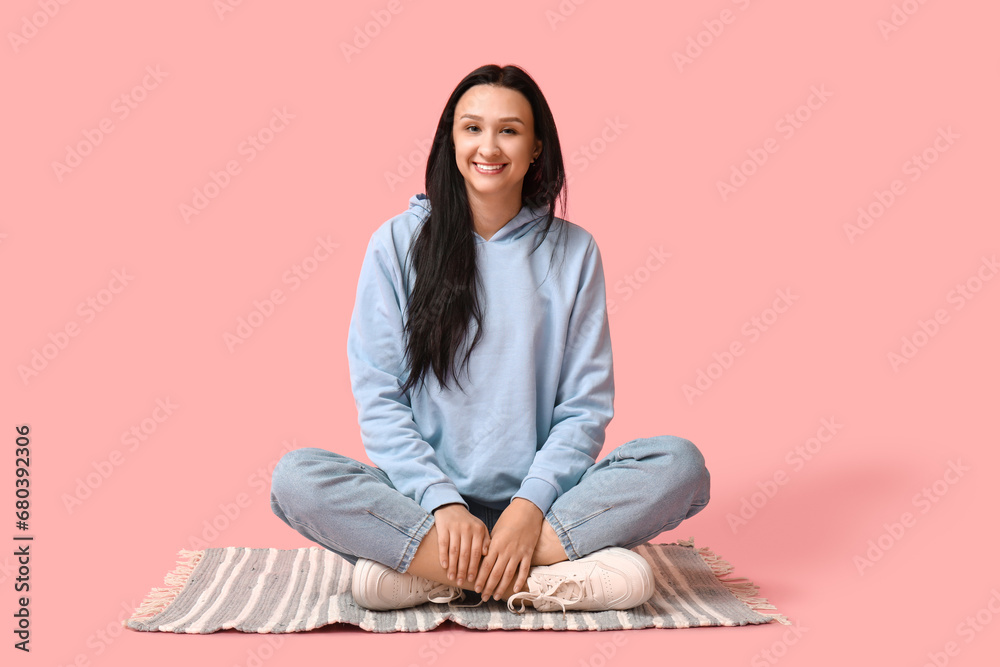 Beautiful young woman sitting on pink background