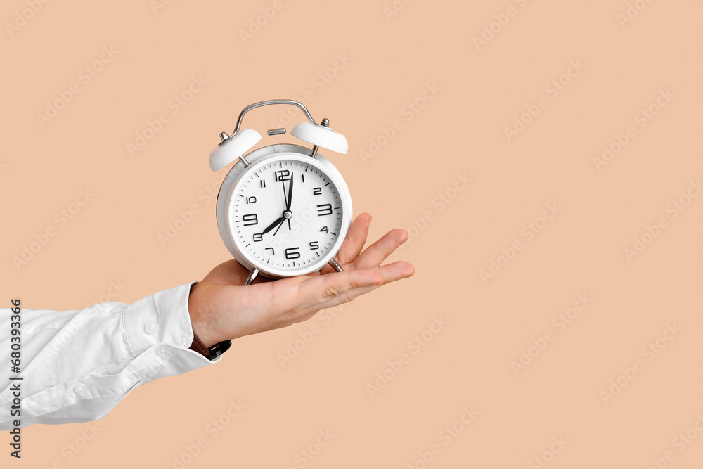 Male hand with alarm clock on beige background. Time management concept