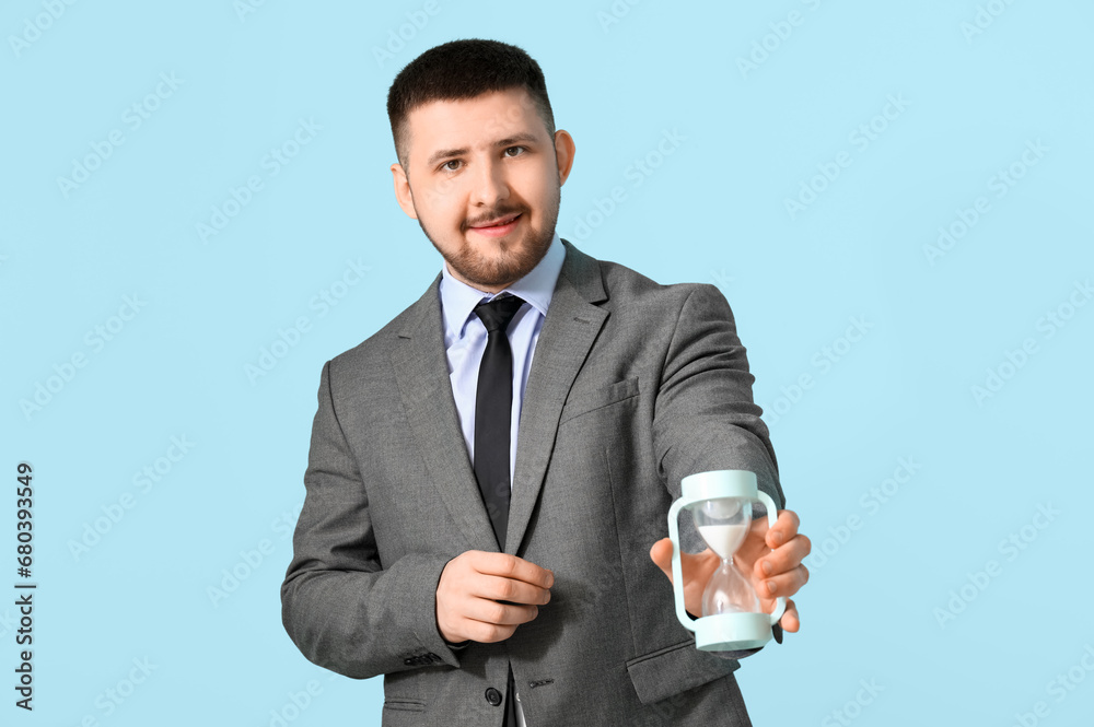 Young happy businessman with hourglass on blue background. Time management concept