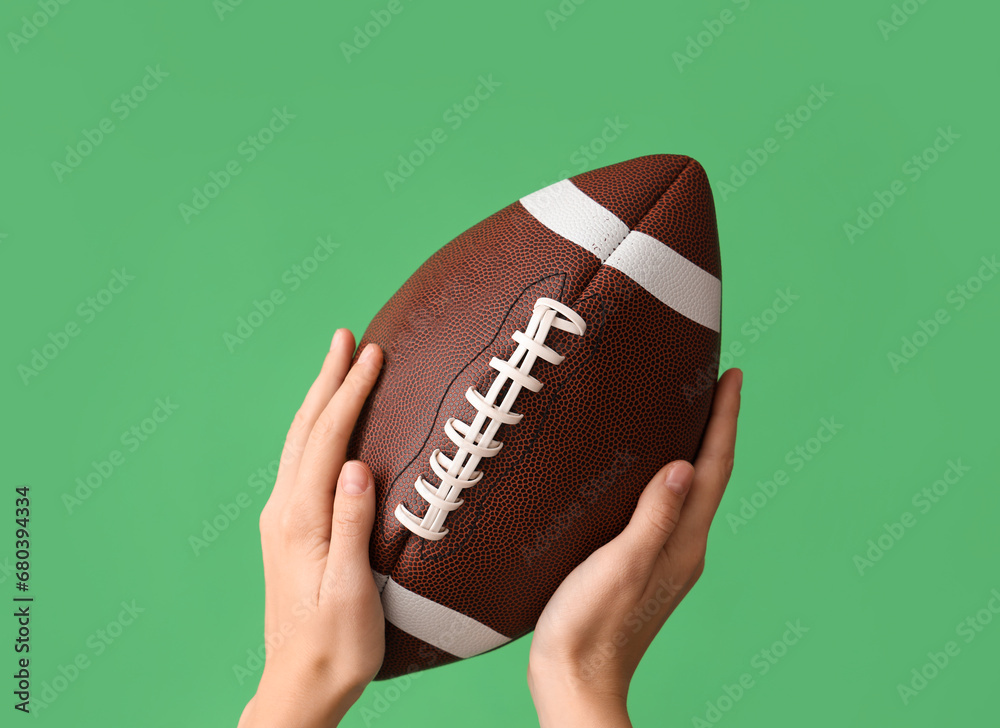 Female hands with ball for American football on green background