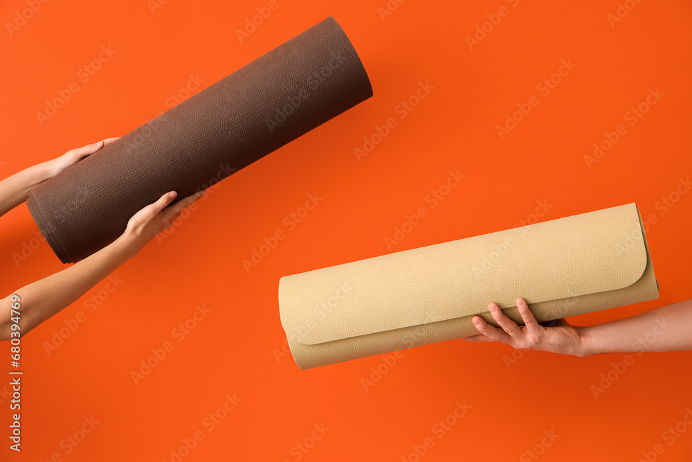 Female hands with yoga mats on orange background