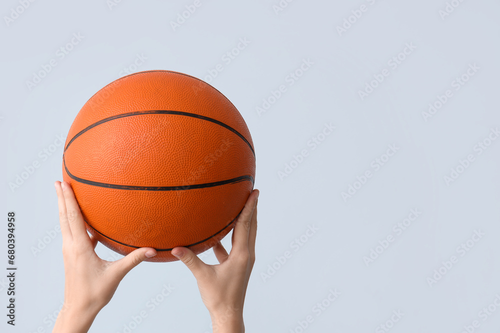 Female hands with ball for playing basketball on grey background