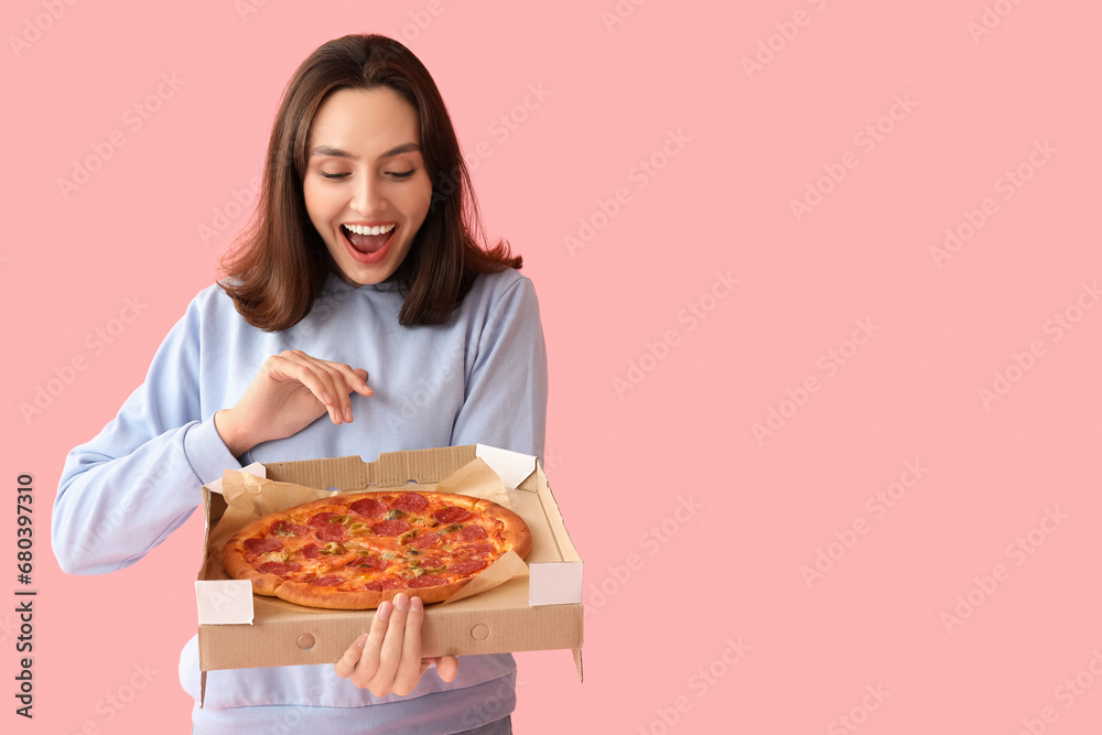 Happy young woman holding cardboard box with tasty pizza on pink background