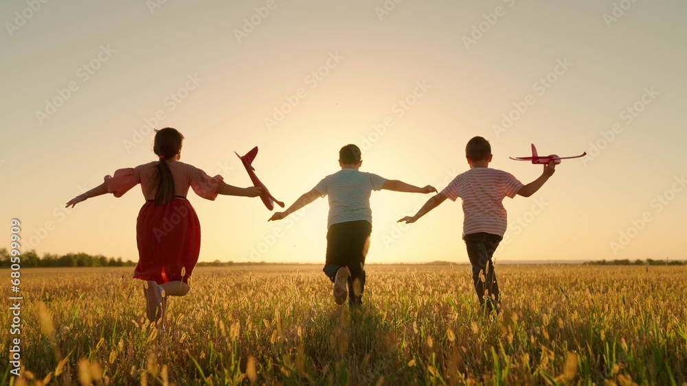 Happy children run with toy plane across field at sunset. Boy, girl wants to become pilot, an astronaut. Children play with toy plane. Slow motion. Teenager dreams of flying, becoming pilot. Childrens