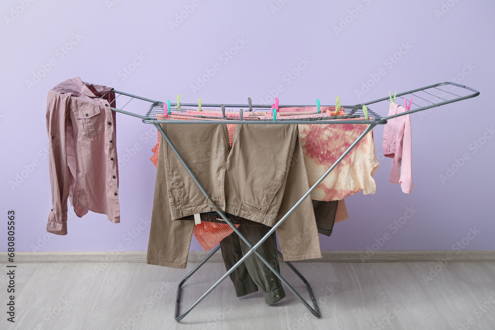 Clean clothes hanging on dryer near lilac wall