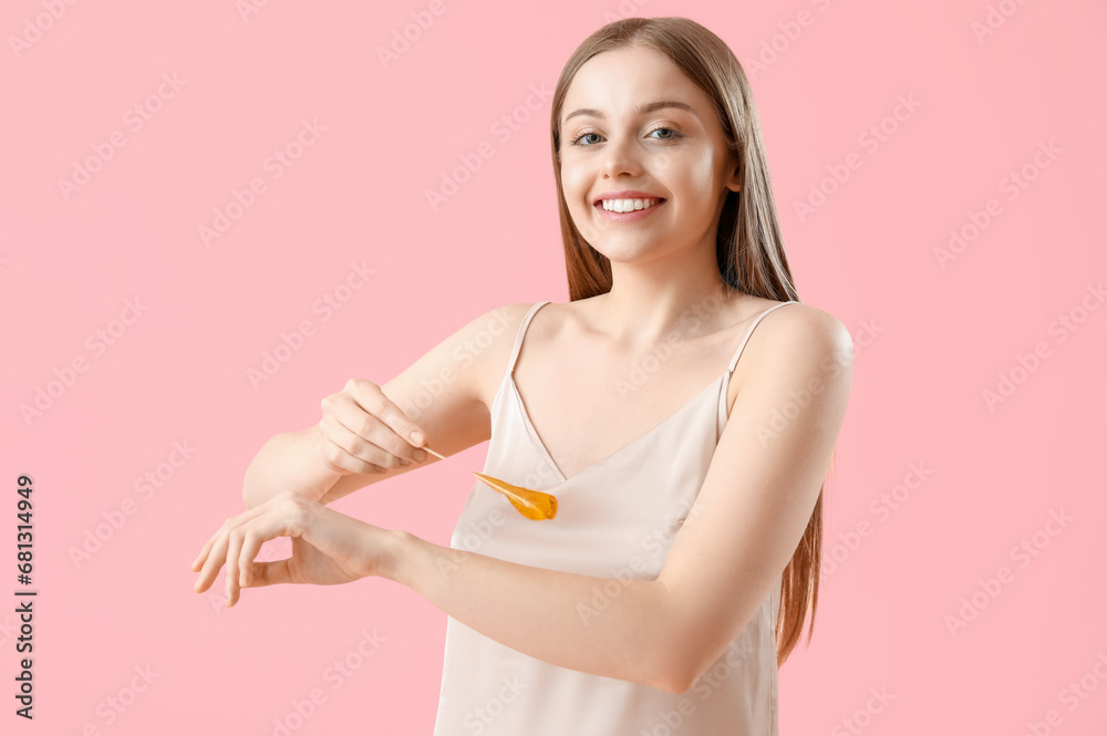 Young woman applying sugaring paste onto her arm against pink background