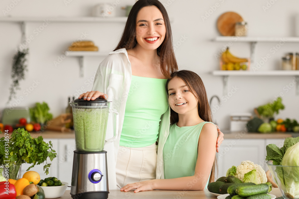 Little girl and her mother making vegetable smoothie with blender in kitchen