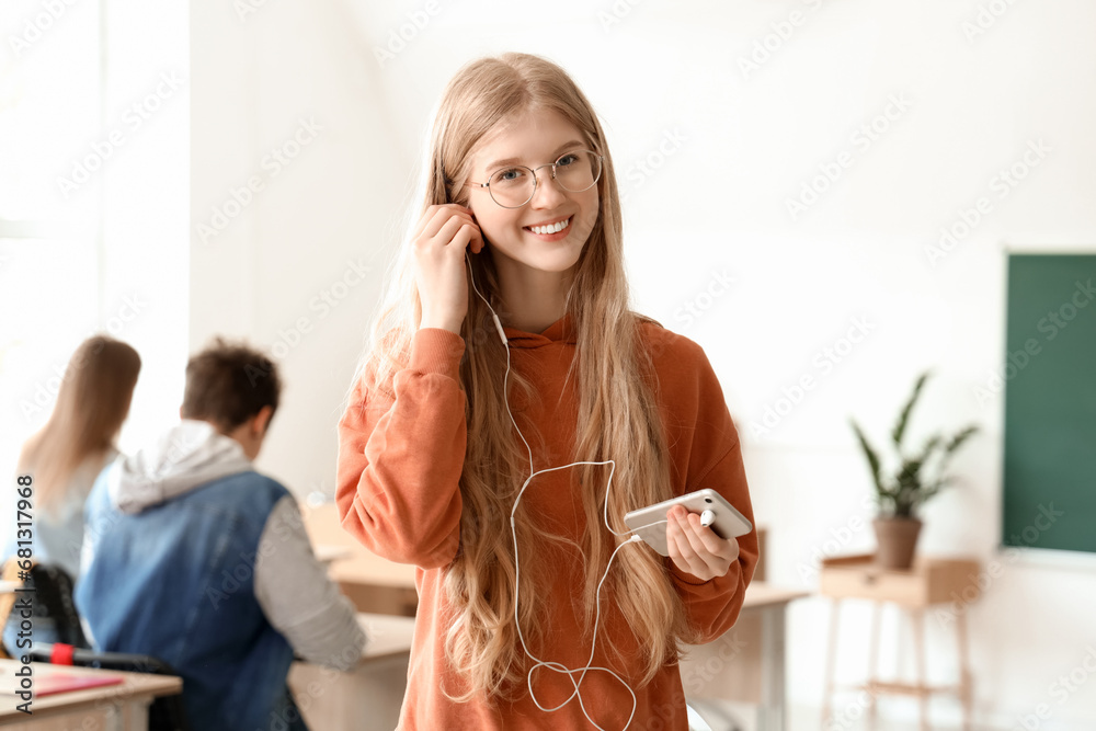 Female student with mobile phone and earphones in classroom