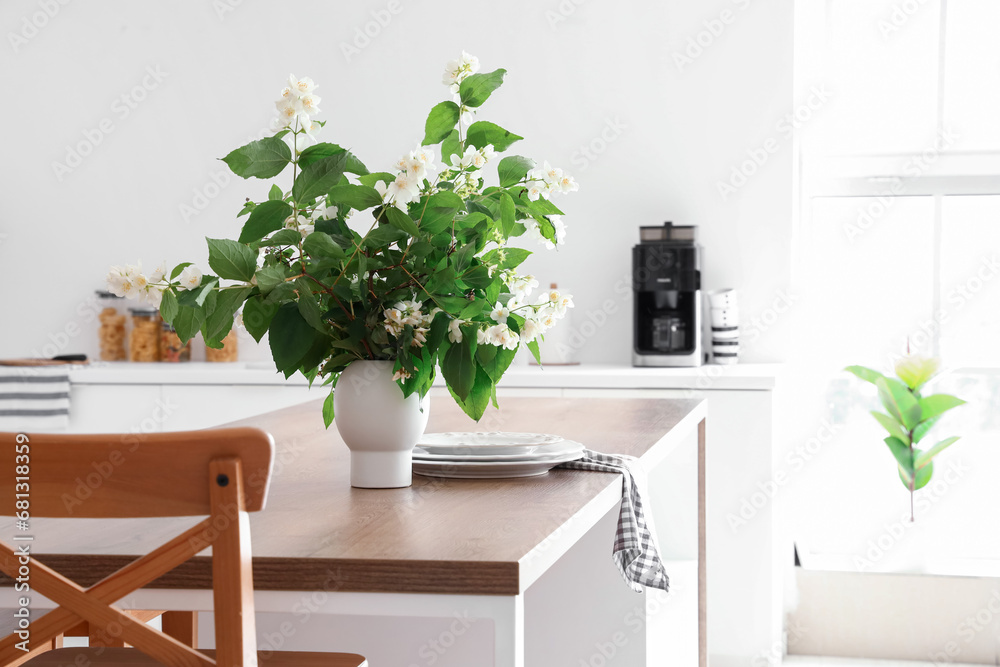 Vase with blooming jasmine flowers on wooden table in modern kitchen