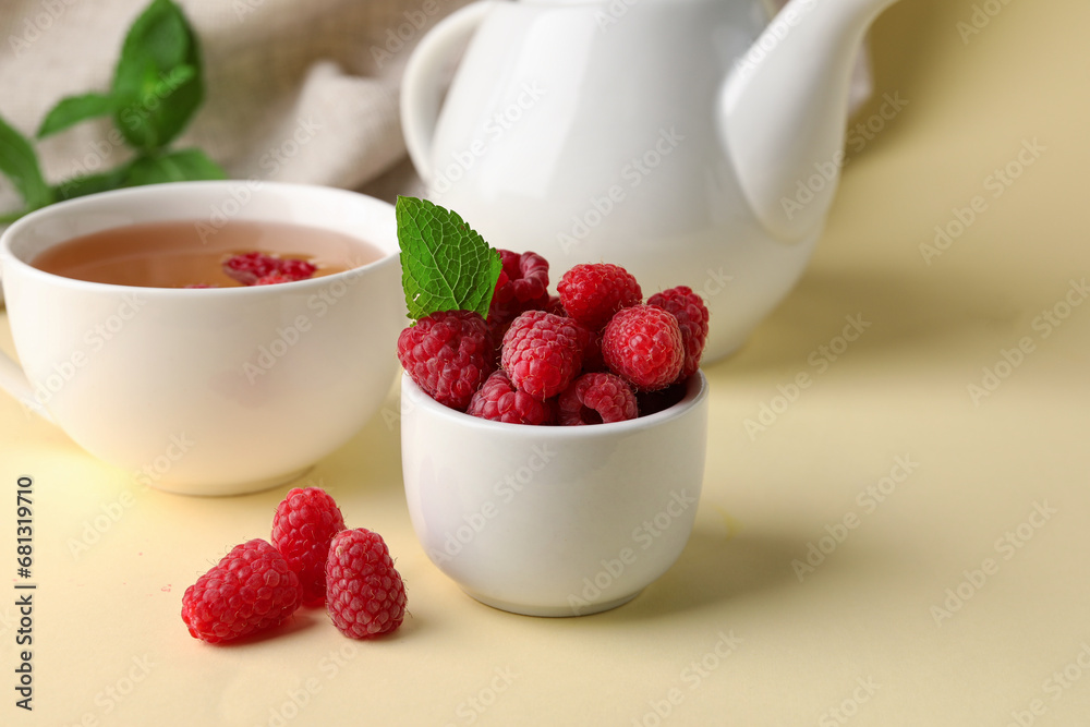 Bowl with fresh raspberries and cup of tea on yellow table