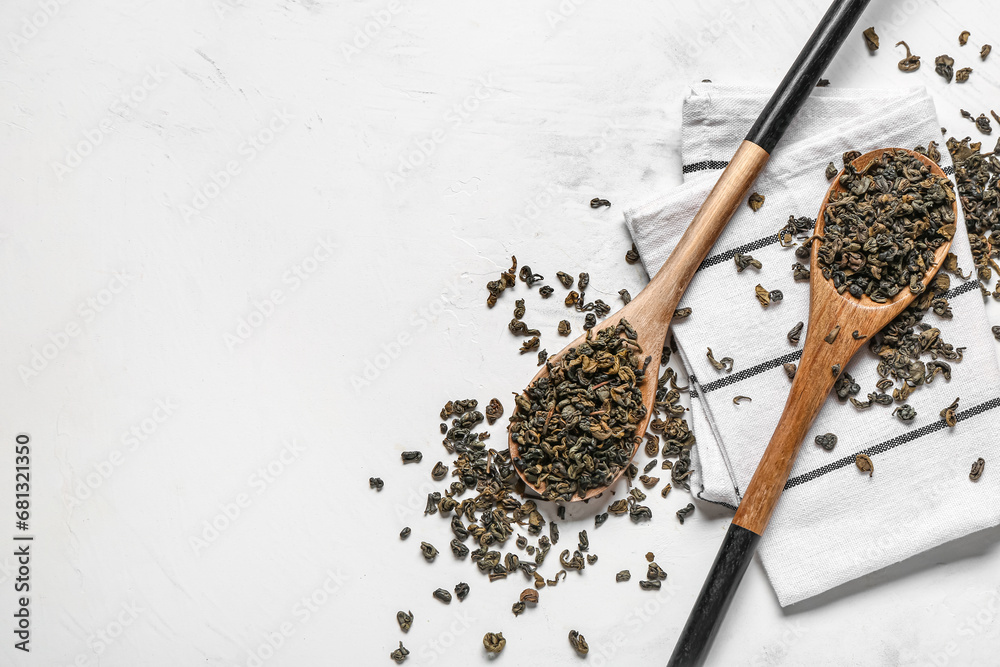 Wooden spoons with dry green tea and towel on white background