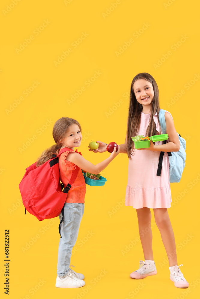 Happy girls with apples and lunchboxes on yellow background