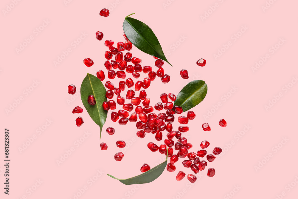 Flying fresh pomegranate seeds and leaves on pink background