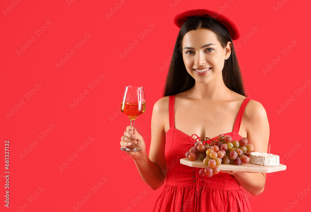 Young woman with glass of wine and grapes on red background