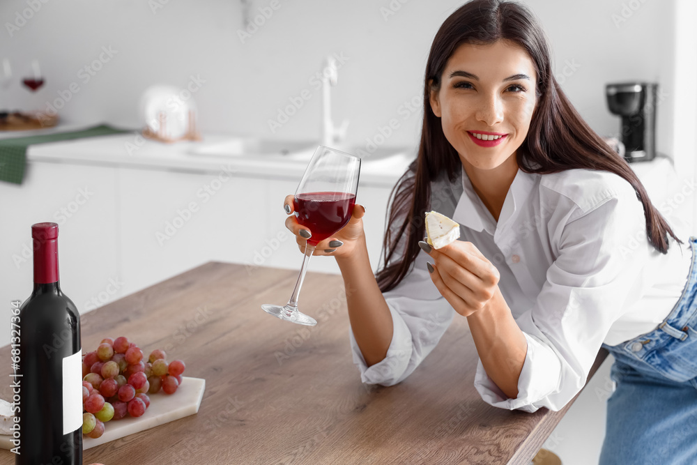 Young woman with glass of wine and cheese in kitchen