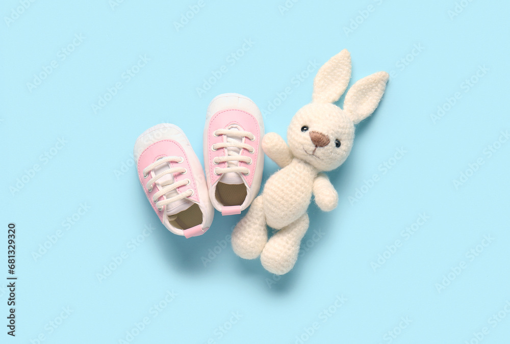 Stylish baby shoes with cute toy on blue background