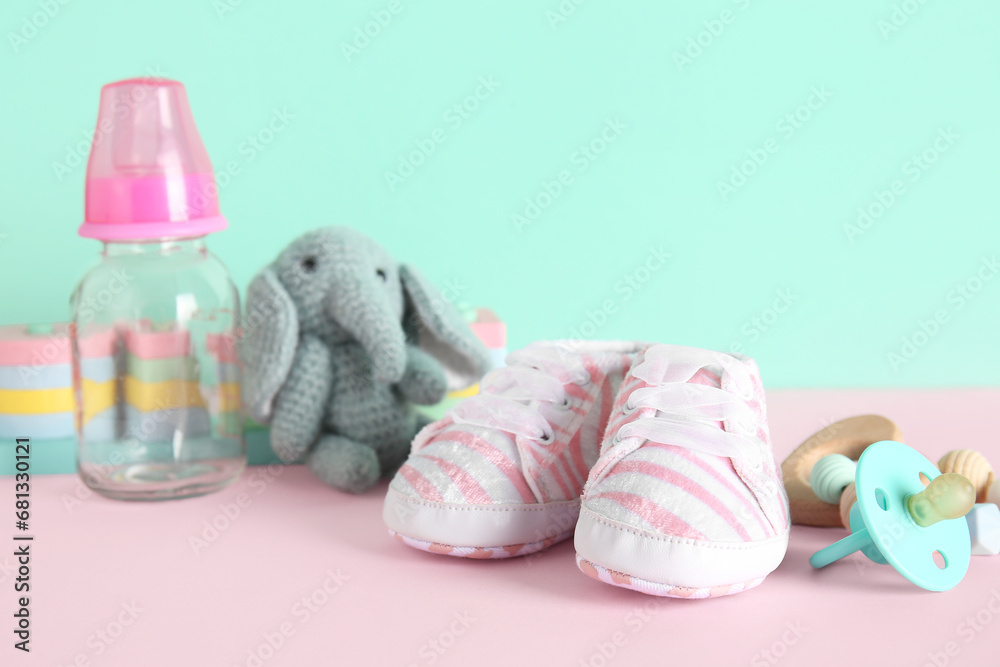 Stylish baby shoes with bottle of milk, toys, pacifier and rattle on color background