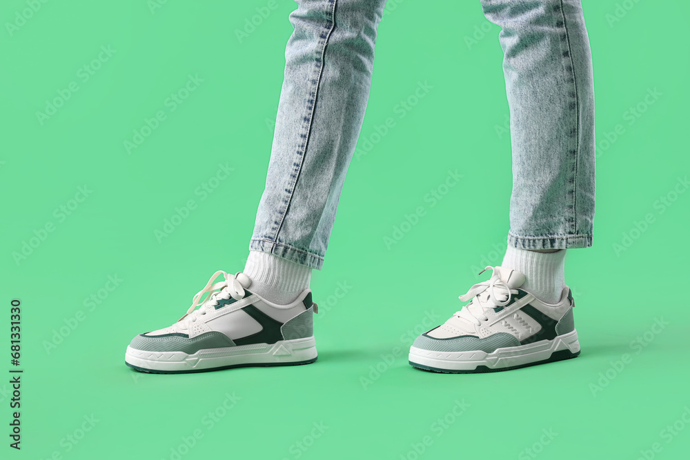 Legs of young woman in stylish sneakers on green background