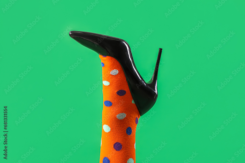 Leg of young woman in stylish black high heel on green background