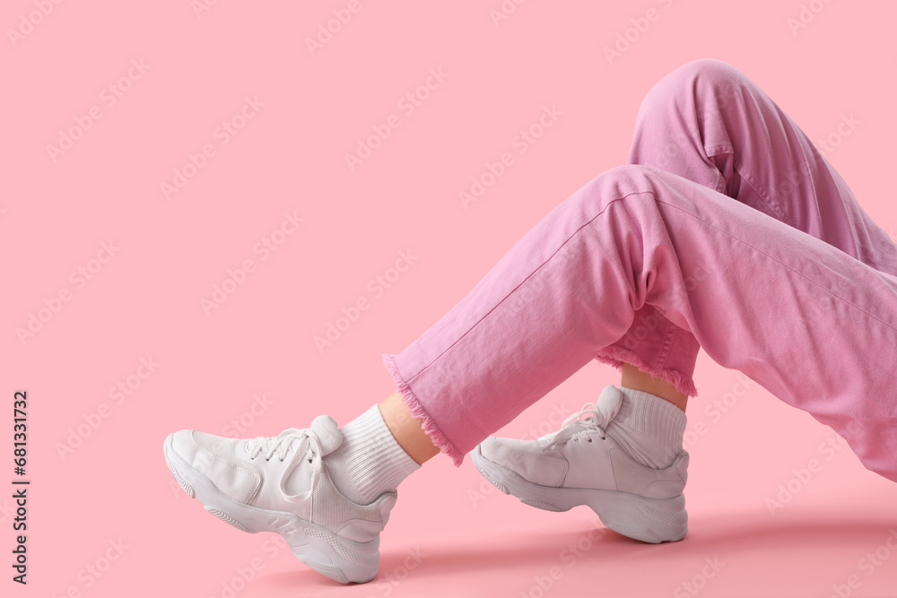 Legs of young woman in stylish white sneakers on pink background