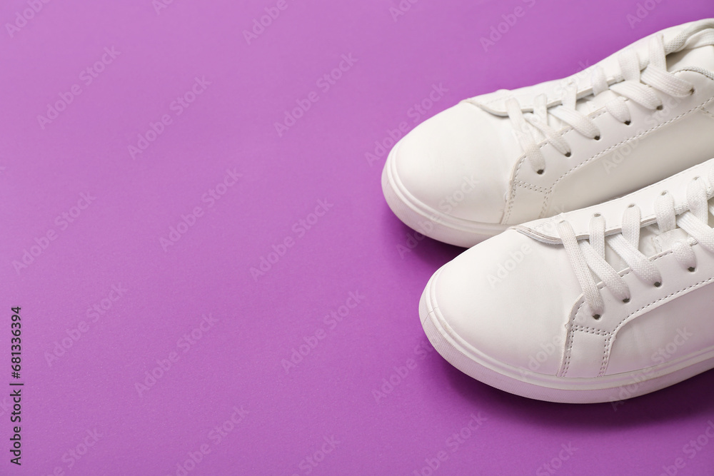 Stylish white sneakers on purple background