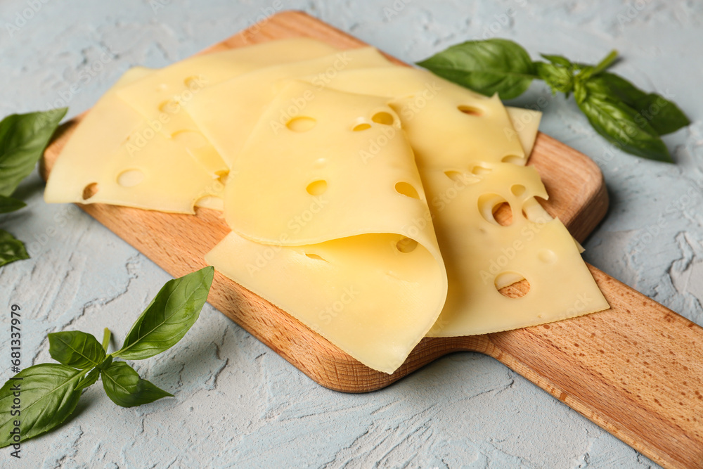 Board with tasty cheese slices and basil leaves on light background, closeup