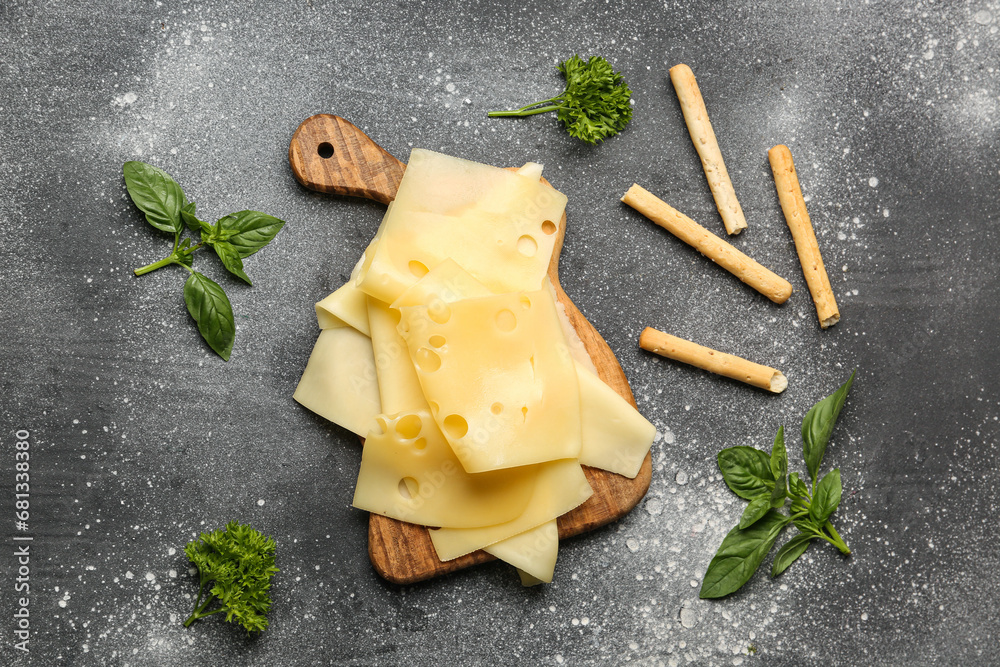 Board with tasty cheese slices, basil leaves and Italian Grissini on grey background